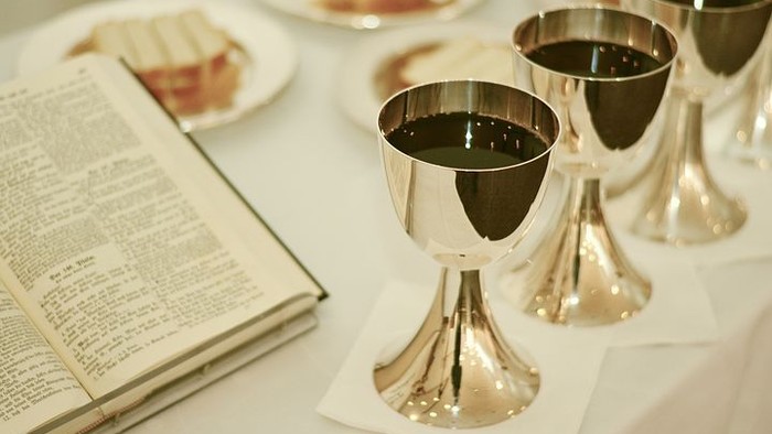 Drei silberne Kelche mit Wein neben einem aufgeschlagenen Buch auf einem Tisch