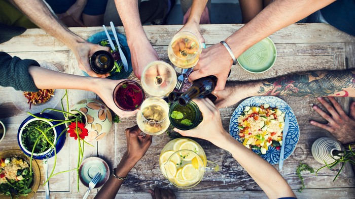 Freunde stoßen mit Getränken an einem Tisch mit verschiedenen Gerichten an