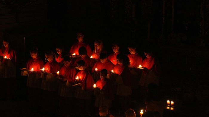 Personen in roten Jacken halten Kerzen in der Dunkelheit
