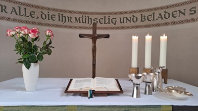 Ein Tisch mit Kreuz, Bibel, Kerzen, Blumen und einem Taufbecken