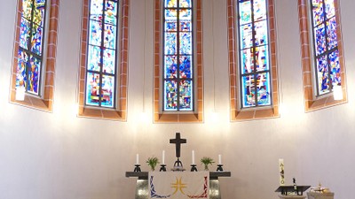 Elegante Kapelle mit Innenraum, der farbige Kirchenfenster, einen Altar mit Kreuz und einen roten Teppichgang zeigt.
