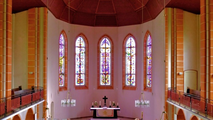 Innenraum einer Kirche mit Altarraum und farbigen Fenstern