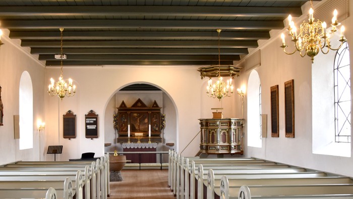 Indre del af kirke med hvidt indretning og hængende lygter