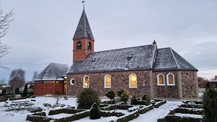 En lille kirke med tårn og murstensmurer i sneklædt landskab