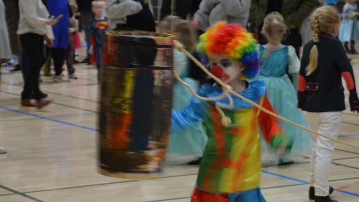 Barn i farverigt tøj danser med stang i sportshal.