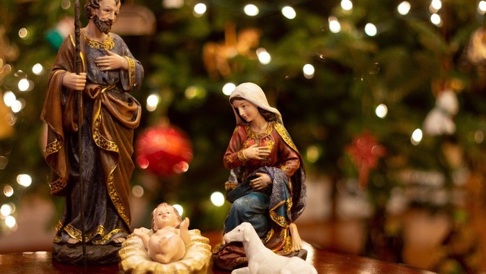 Eine Weihnachtskrippe mit Maria, Josef und Baby Jesus vor einem beleuchteten Weihnachtsbaum.