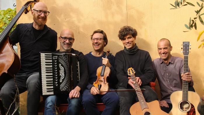 Fünf Männer posieren mit Musikinstrumenten und lächeln.