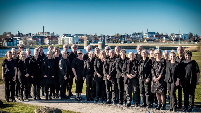En gruppe af kvinder i mørke klæder står sammen udendørs med en by i baggrunden