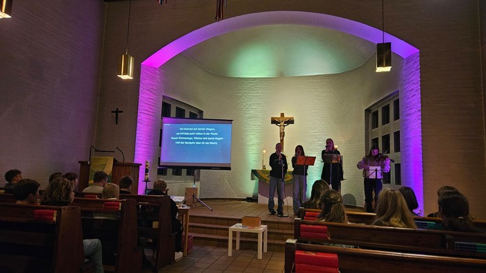 In der Kirche findet eine Veranstaltung statt, Menschen stehen vor einem Bildschirm und einem Kreuz.