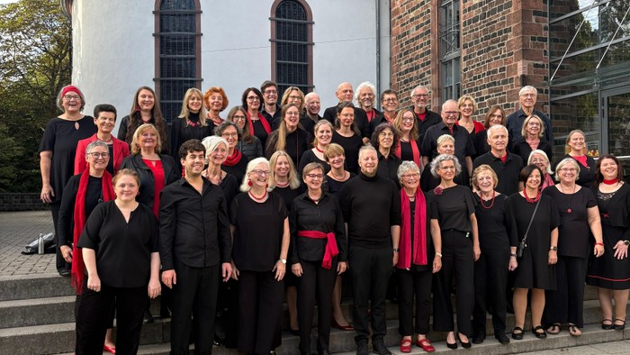 Eine vielfältige Gruppe von Menschen in einheitlicher schwarzer Kleidung posiert vor einem historischen Kirchengebäude.