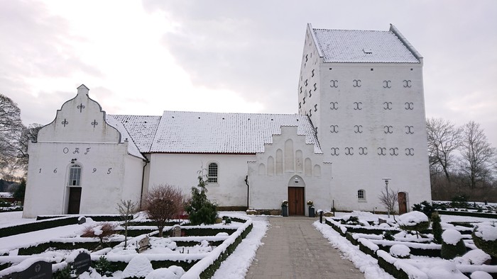 En snedækket kirke med tårn og sideskib i vinterlandskab