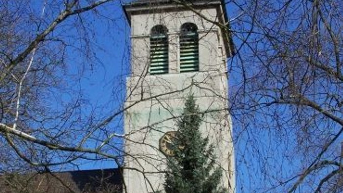 Ein hoher weißer Turm mit schwarzem Dach und Uhr, umgeben von kahlen Bäumen und einem blauen Himmel