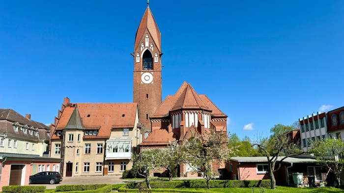 Bild zeigt eine Kirche mit hohem Turm und Uhr, umgeben von einem gepflegten Garten.