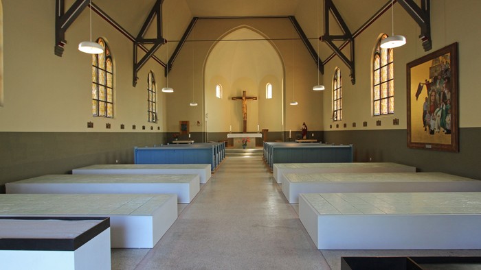 Ein leerer Kirchenraum mit weißen Bänken und einem Kreuz am Altar