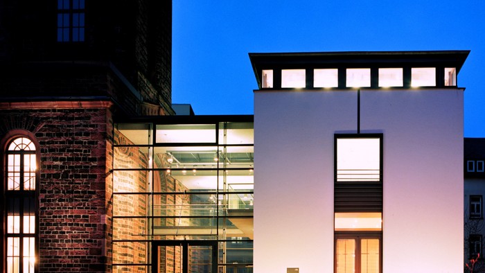 Modernes Gebäude mit Glasfront und Treppe, daneben alter Backsteinturm