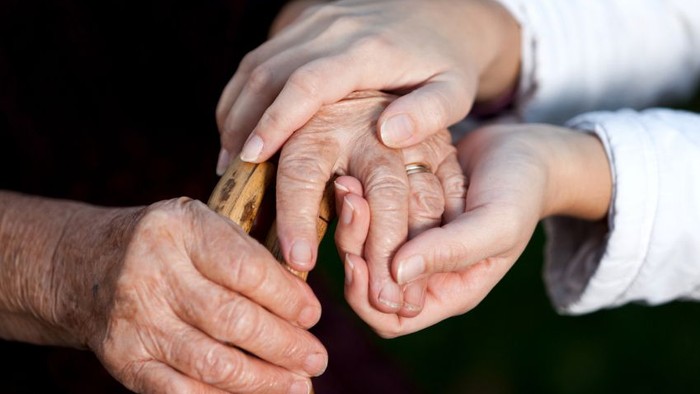 En blid hånd støtter en ældre person, der holder en stok, og viser omsorgsfuld hjælp og fællesskab.