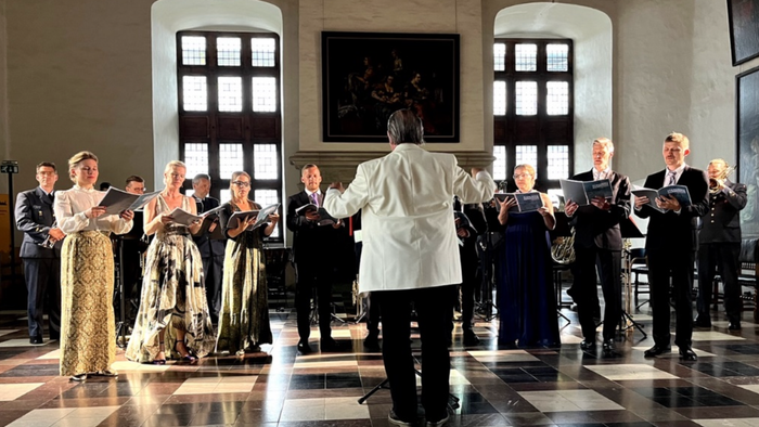 Et kor optræder i en stor sal med en dirigent, der leder.