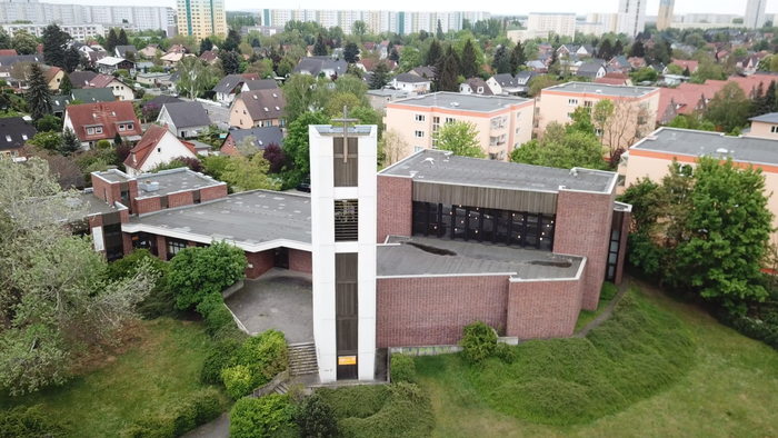 Ein modernes Kirchengebäude mit hohem Kreuz inmitten von Grünflächen und Wohnhäusern.