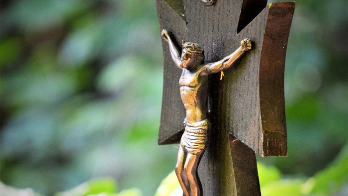 Ein hölzernes Kruzifix hängt an einem Rosenkranz im Garten.