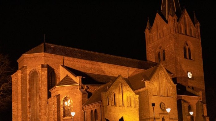 En belyset kirke om natten med lys omgivet af en hegn.