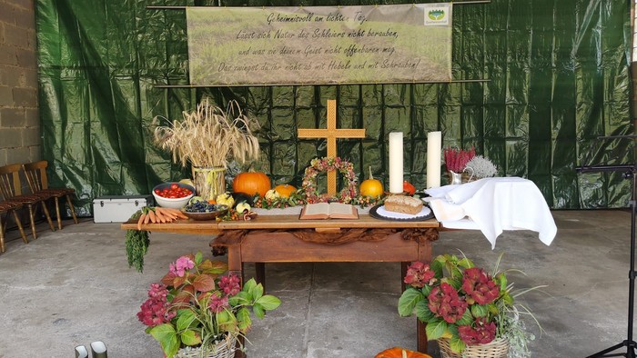 Ein Tisch mit Kreuz, Kerzen, Kürbissen und Blumen vor grünem Hintergrund