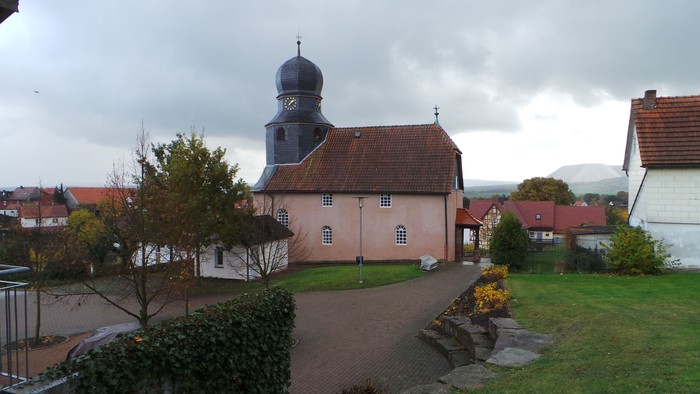 Ein Kirchengebäude mit schwarzer Kuppel und Uhr, umgeben von grünem Rasen und anderen Häusern.