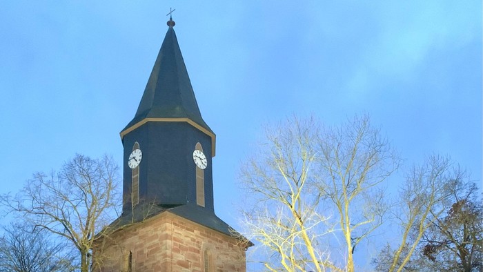 Kirchturm mit Uhr und spitzen Dach bei Dämmerung