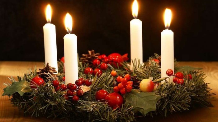 En adventskranse med fire lyse lygter, grønne blade og røde bær.