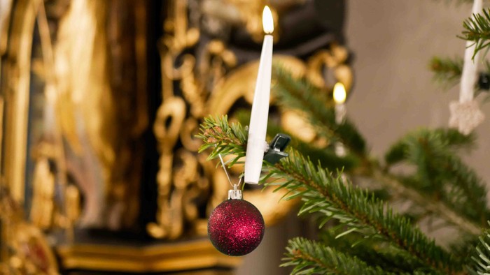 En tændt lysestage hænger fra en juletræsgren med en rød julekugle.