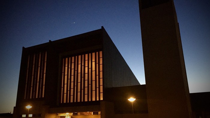En stor, moderne bygning med mange vinduer og en høj tårn ved natten