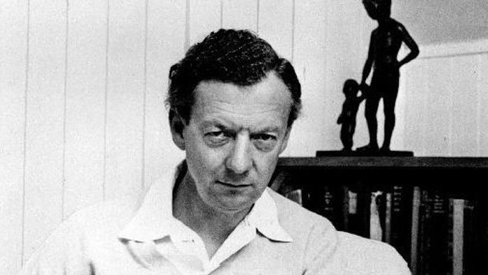 Mand, der læser en bog i et rum med en statue bag sig.