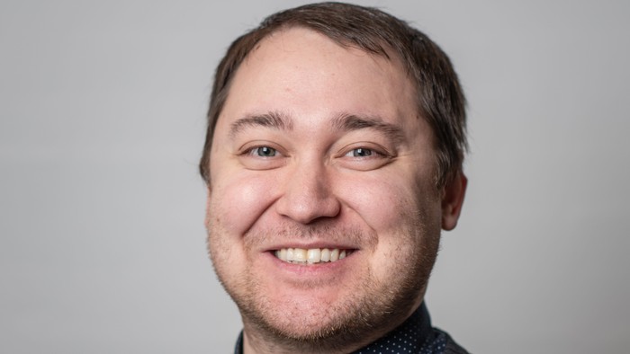 En smilende mand med kort hår og stribet trøje.