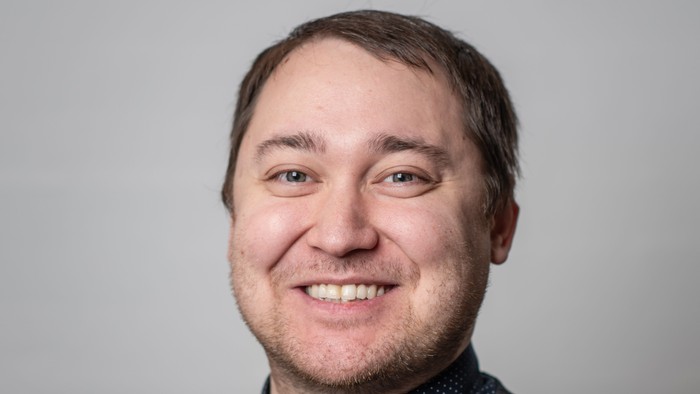 En smilende mand med kort hår og stribet trøje.