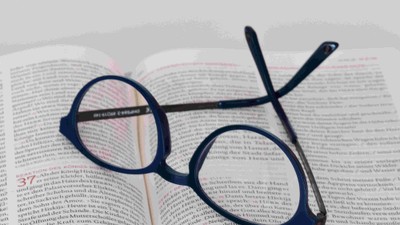 Brille und Stift auf aufgeschlagenem Buch