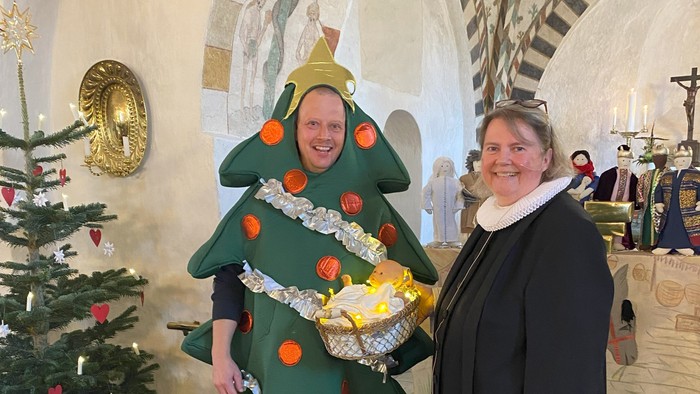 En person i juletrædragt står sammen med en annen person i kirke.
