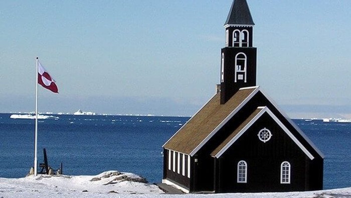 Sort kirke ved havet med dansk flag.