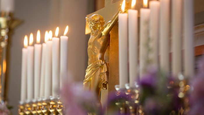 En gylden crucifix med lysende lys og violette blomster i forgrunden