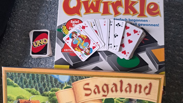 Drei Brettspiele und ein UNO-Kartenspiel auf einer Oberfläche ausgelegt, darunter Qwirkle, Sagaland und ein verpacktes UNO-Set.