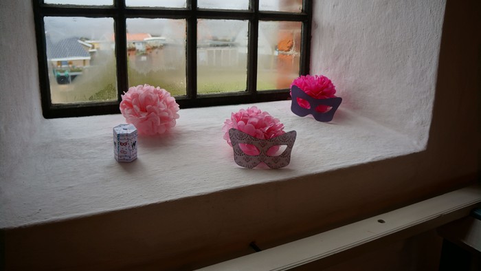 En vindueskarm med tre rosa papirblomster og en lille kasse med nøgler.