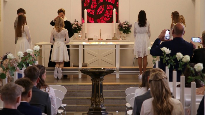 En bryllupsceremoni finder sted i en kirke med gæster, brudefoljet og præst ved alteret.