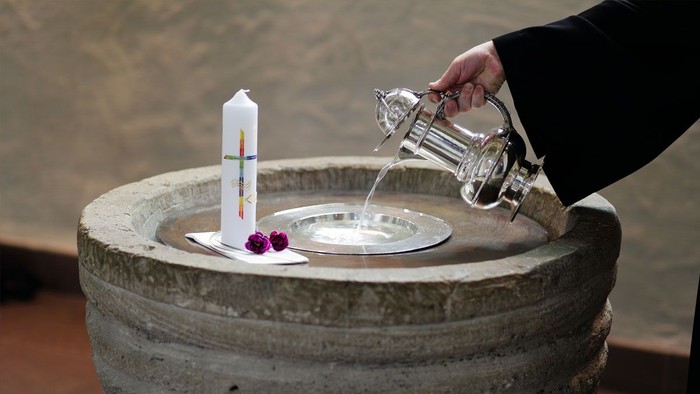 Eine Person gießt Wasser in ein steinernes Becken mit einer Kerze und einem Teller, wahrscheinlich für ein Segnungsritual.