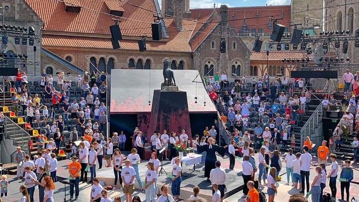 Eine große Menschenmenge versammelt sich zu einem Open-Air-Konzert mit Künstlern auf der Bühne auf einem historischen europäischen Platz.