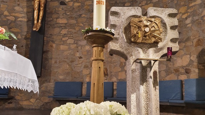 Weiße Blumen vor Kreuz und Kerze in Kirche