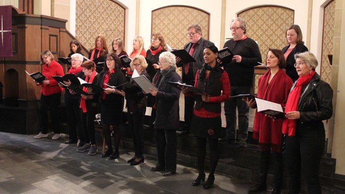 Eine Gruppe von Menschen in passender roter Kleidung, die gemeinsam in einer Kirche singen.
