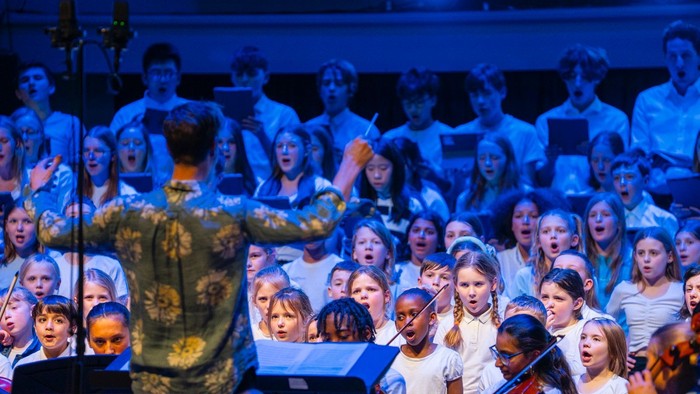 Ein großer Jugendchor tritt leidenschaftlich auf der Bühne auf, während ein Dirigent sie anführt.