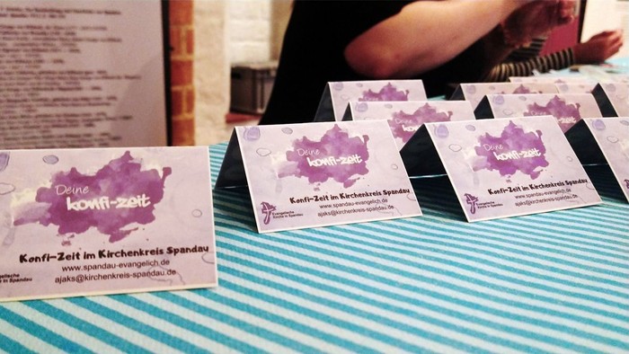 Mehrere Visitenkarten mit lila Design liegen auf einem blau gestreiften Tisch.