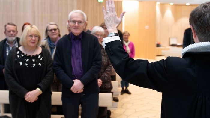 En gruppe mennesker i formel klædning deltager i en seremoni i et rum med trævægge og benker.