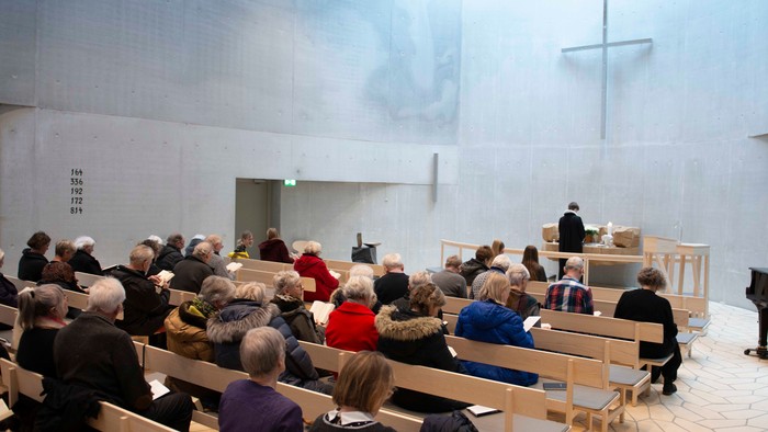 En gruppe mennesker sidder i en kirke og lytter til en prædiken.