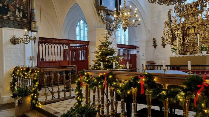 Køge Kirke set indefra i juletiden. Balustrene er pyntet med granguirlander med lys og røde sløjfer.