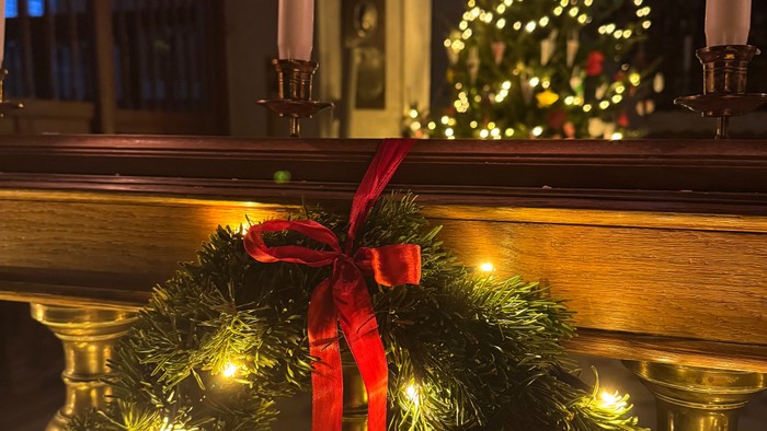 En juletidskærede med lys og rød bue foran en lyset kælderkammer med lysende juletræ og lyse candlesticks